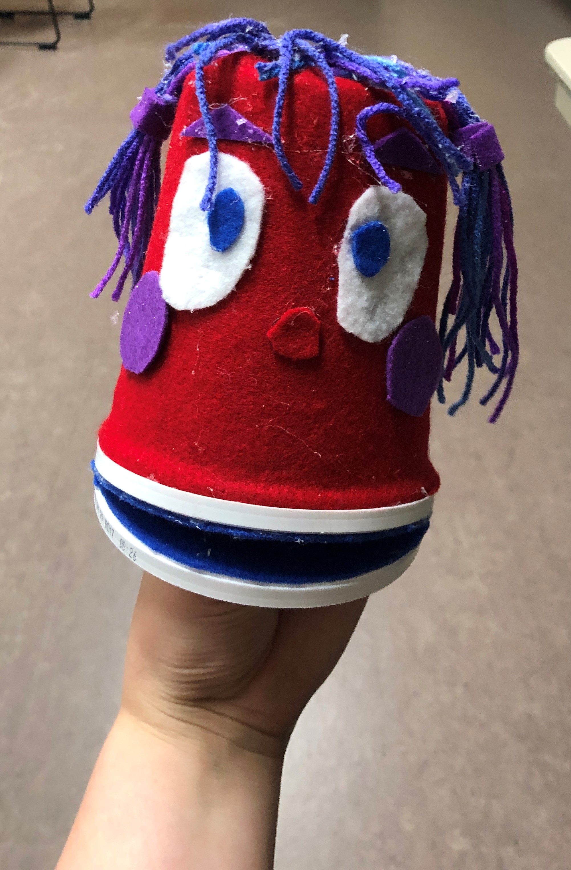 a hand puppet with a cartoon face with red skin and purple hair