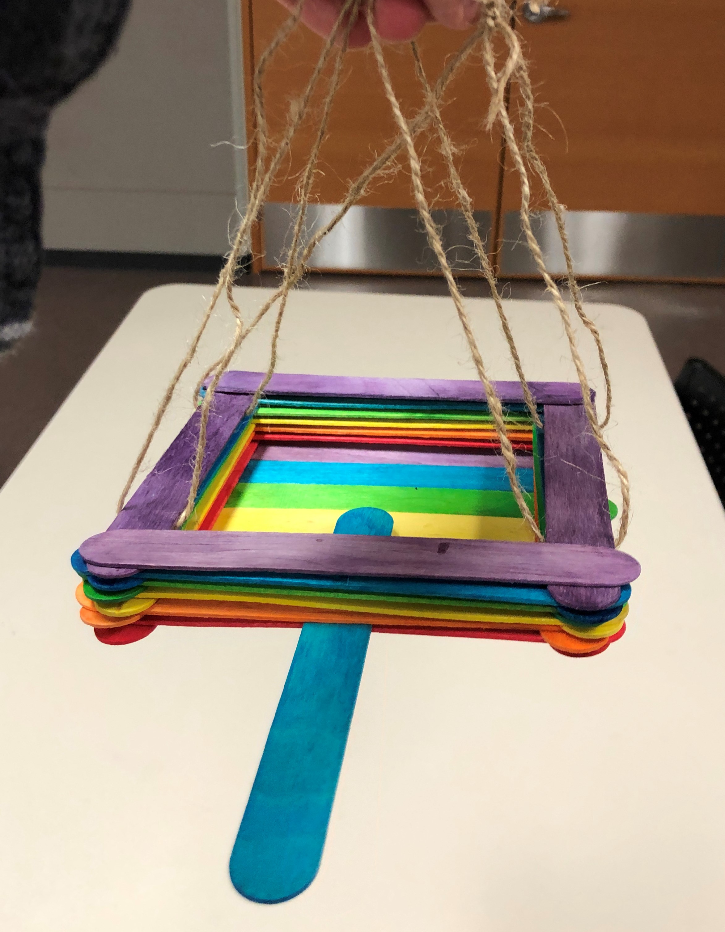 rainbow square made out of popsicle sticks, held up by twine