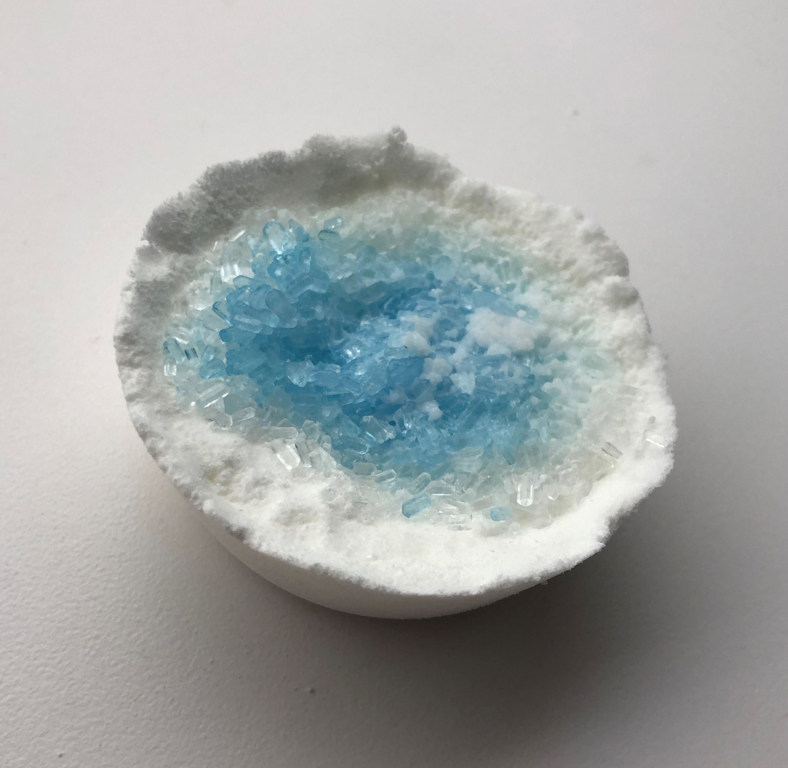 a white bath bomb with blue epsom salts on top