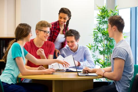 Five teens sitting around a table, laughing and looking at papers