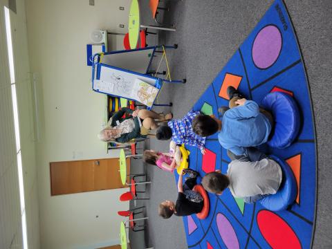 children sitting on a rug as programmer shows them a storybook, drawing, and information about ants